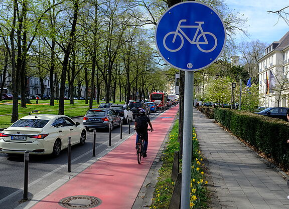 Landesversammlung_ADFC_NRW_2025._ADFC_NRW__B._Glitz___96_.JPG Ein geschützter Radfahrstreifen mit Roteinfärbung. Radwegschild und einer Radfahrerin.