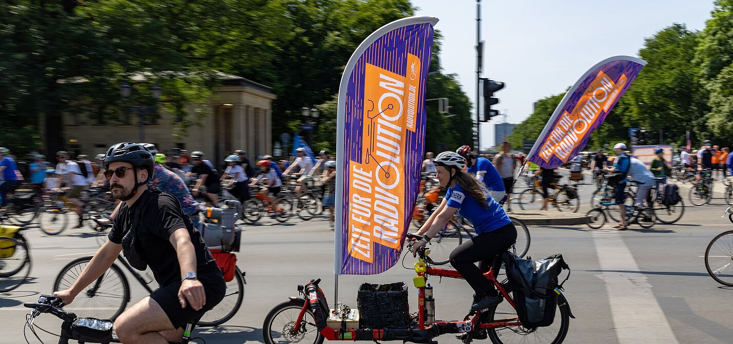 ADFC-Sternfahrt Berlin 2023 Viele Menschen auf Fahrrädern. An einem Rad befindet sich eine große Fahne mit dem Wort "Radvolution" darauf.