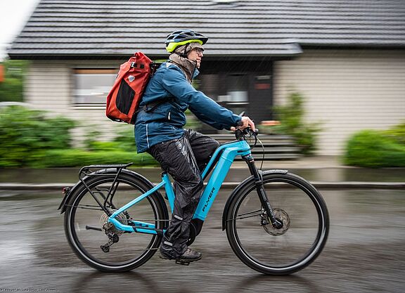 Nässe Radfahrer von der Seite aufgenommen auf Pedelec im Regen unterwegs.