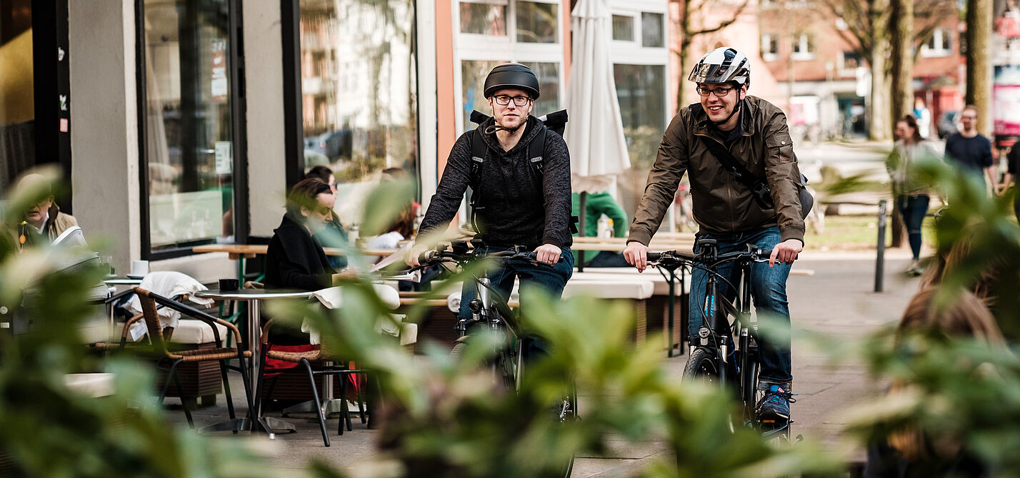 Radfahrer mit Helm Zwei Männer mit Helm fahren auf einem Radweg im urbanen Raum