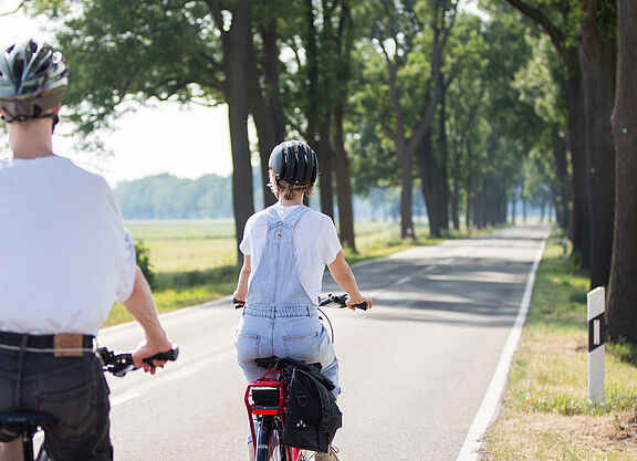 Radfahrende auf einer Landstraße Zwei Personen mit Fahrradhelmen fahren auf einer schmalen Landstraße ohne separaten Radweg.